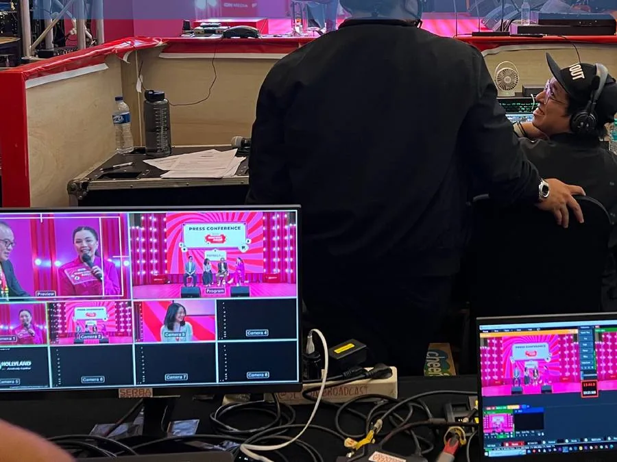 Kru dengan headset mengawasi monitor program di belakang panggung acara.