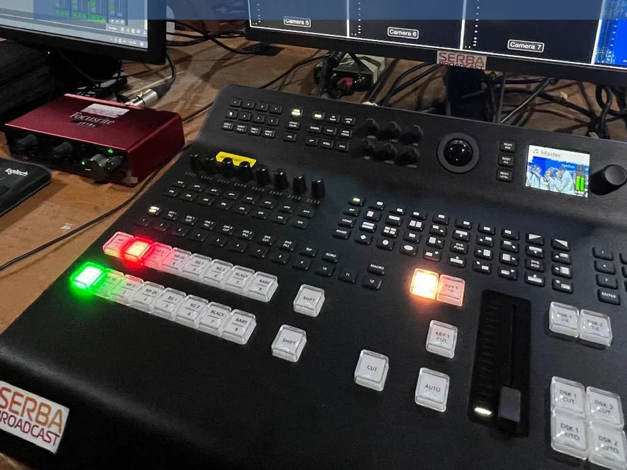 Panel switcher video dengan tombol tally menyala di meja produksi.
